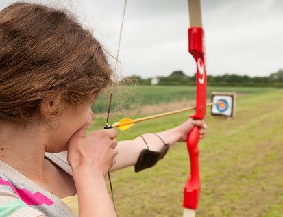 Child holding string back on bow and aim across Archery field
